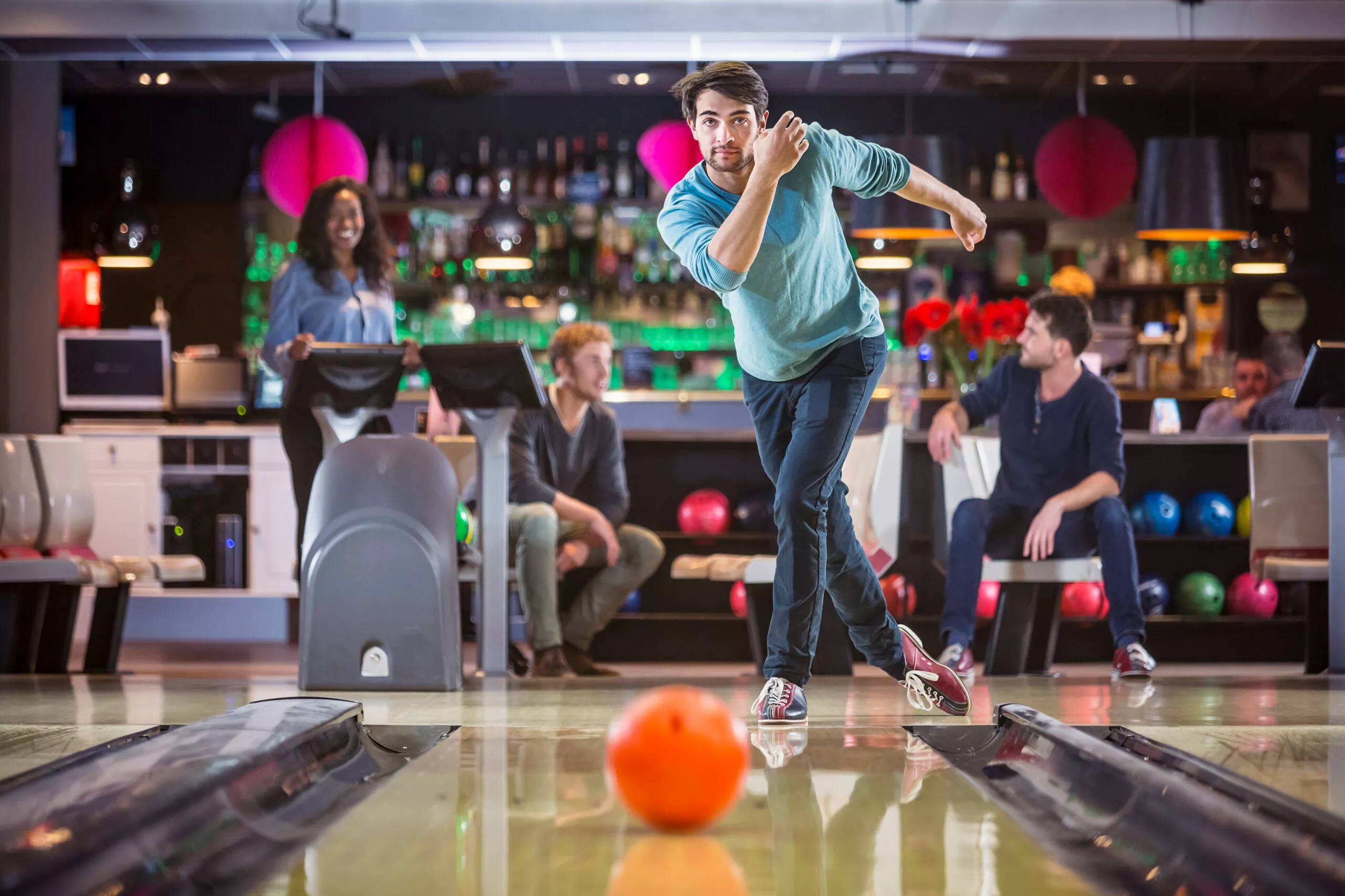 Un giovane uomo sta giocando a bowling con i suoi amici, guardando concentrato